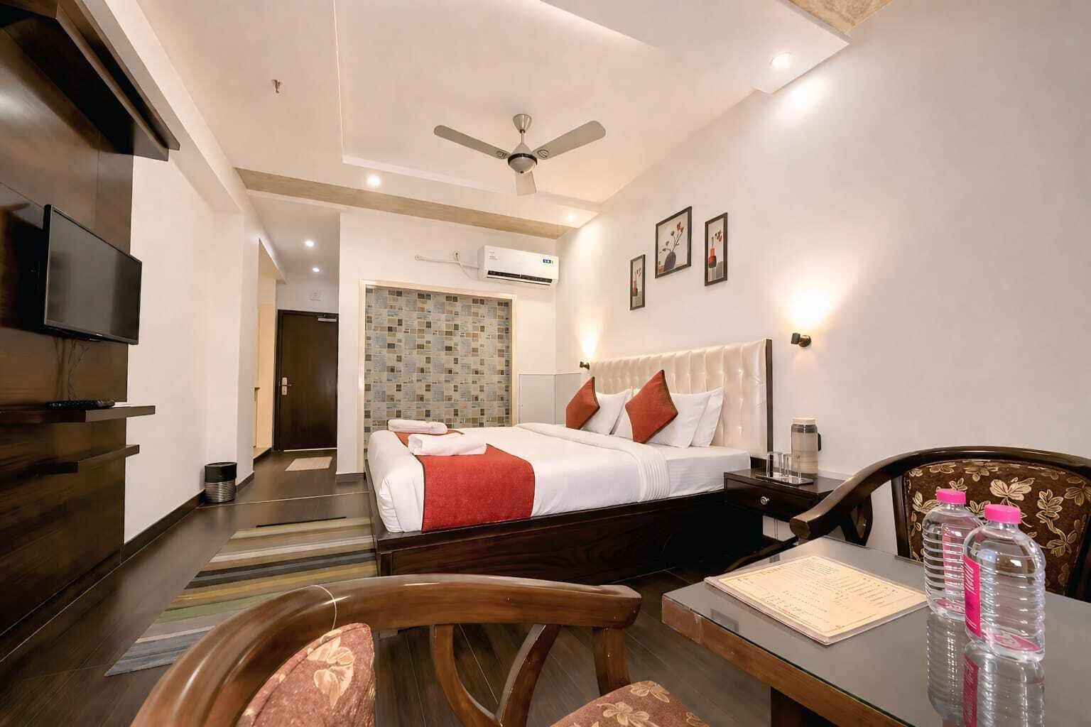 A hotel room with a bed, a desk with a chair, a television, and a ceiling fan.