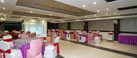A large hall with rows of white chairs and tables, some with pink and purple tablecloths.
