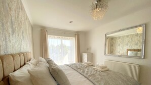 A bedroom with a large bed, a dresser, a mirror, and a chandelier.