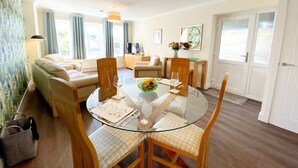 A modern living room with a glass dining table, wooden chairs, a sofa, and a TV.
