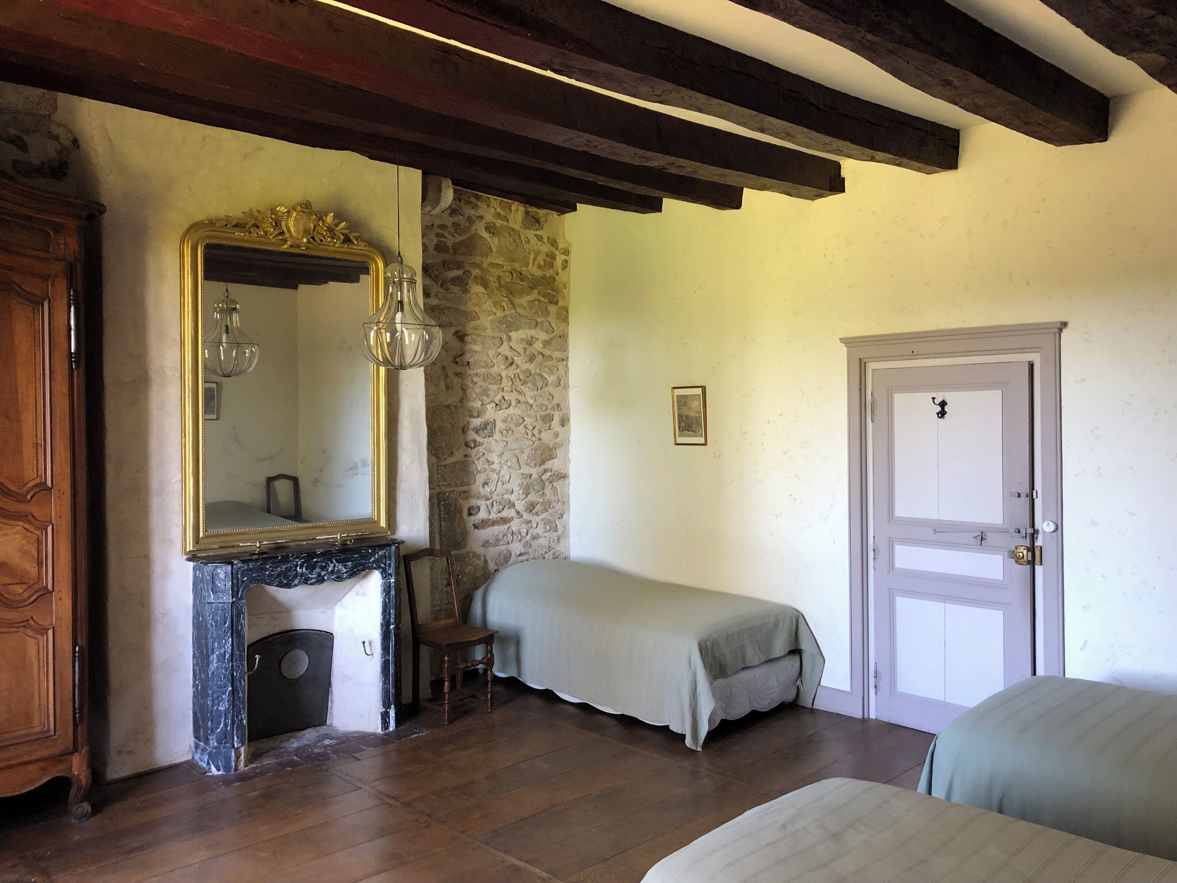 A bedroom with a stone wall, a wooden wardrobe, a marble fireplace, a bed, and a door.