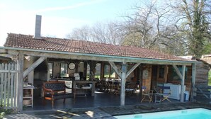 Un espacio al aire libre techado con piscina, muebles de madera y un edificio rústico con tejado de tejas.