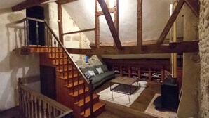 Una habitación rústica con vigas de madera a la vista, un sofá verde, una mesa de centro y una chimenea.