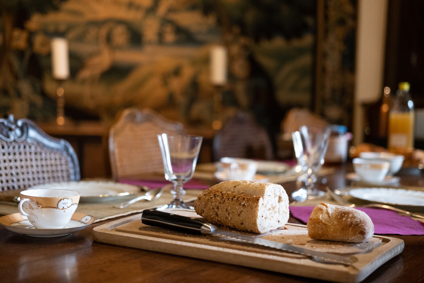 A dining table with a loaf of bread, a pastry, and a cup on a saucer.