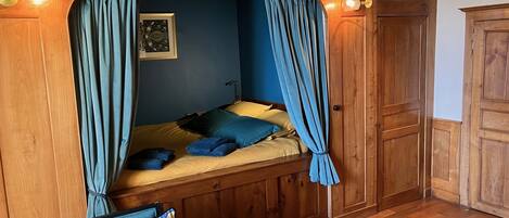 Una habitación acogedora con cama, paredes de madera, una mesita y un armario.