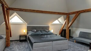 Une chambre avec un plafond en pente, un lit, une table de chevet, une lampe et un canapé.