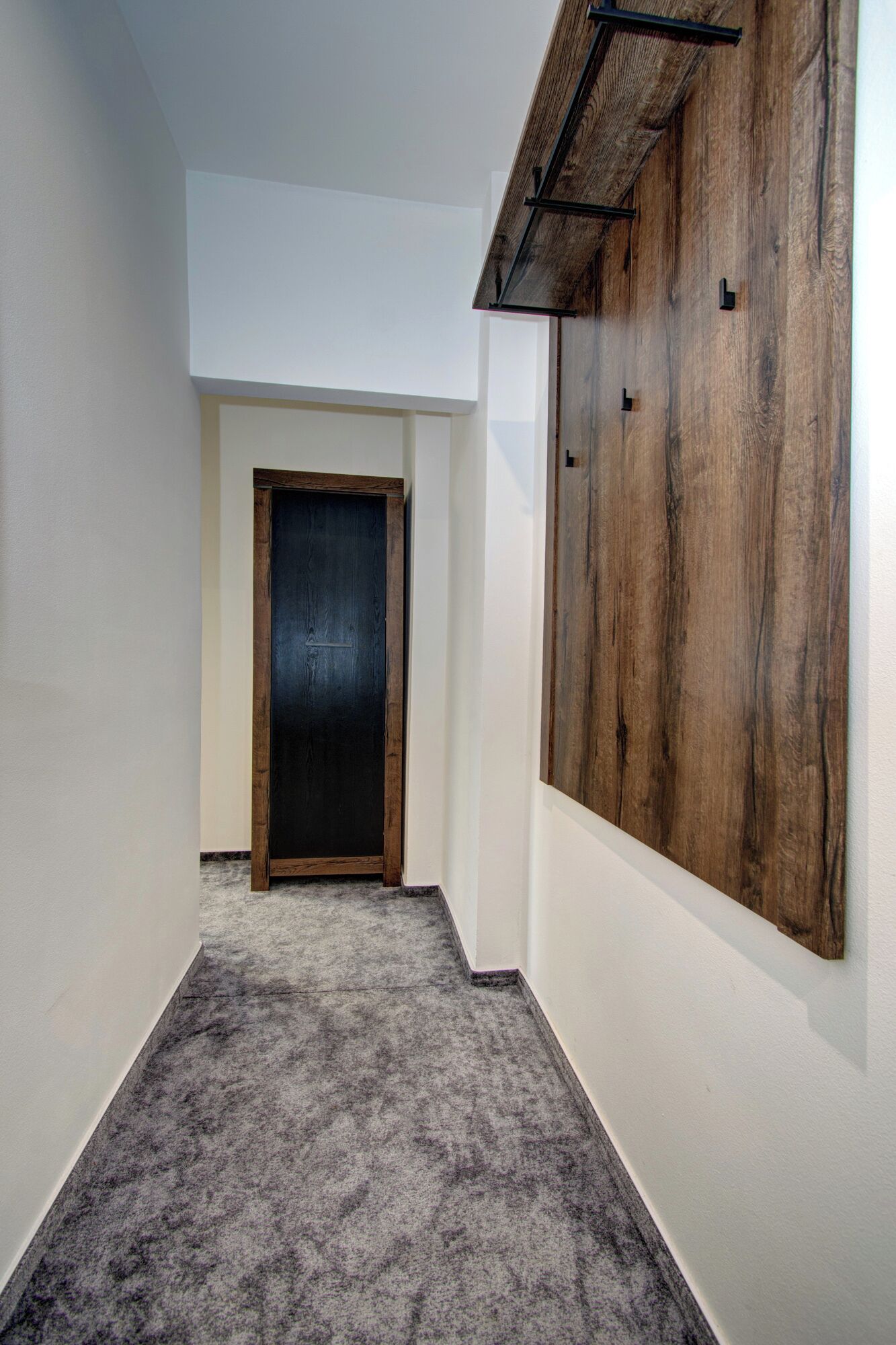 Un pasillo con una puerta de madera oscura, un llamativo panel de madera y suelo alfombrado.