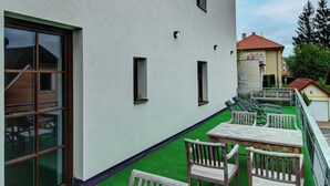 Un bâtiment à l’extérieur blanc, doté de nombreuses fenêtres et agrémenté d’une pelouse artificielle verte ainsi que de chaises en bois.