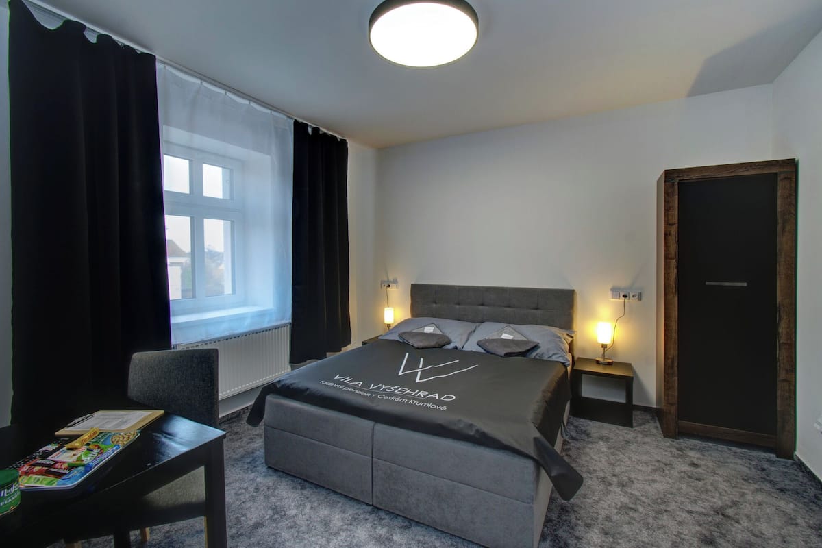 Een moderne slaapkamer met een bed, nachtkastjes, een stoel, een raam met gordijnen en een deur.