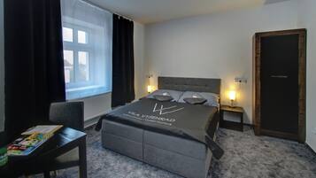 Un dormitorio moderno con cama, mesitas de noche, una silla, un ventanal con cortinas y una puerta.