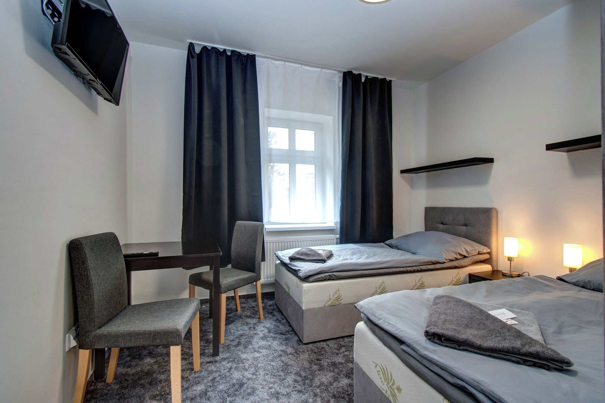 Una camera d'albergo con un letto, una scrivania, una sedia, una televisione e una finestra con tende.