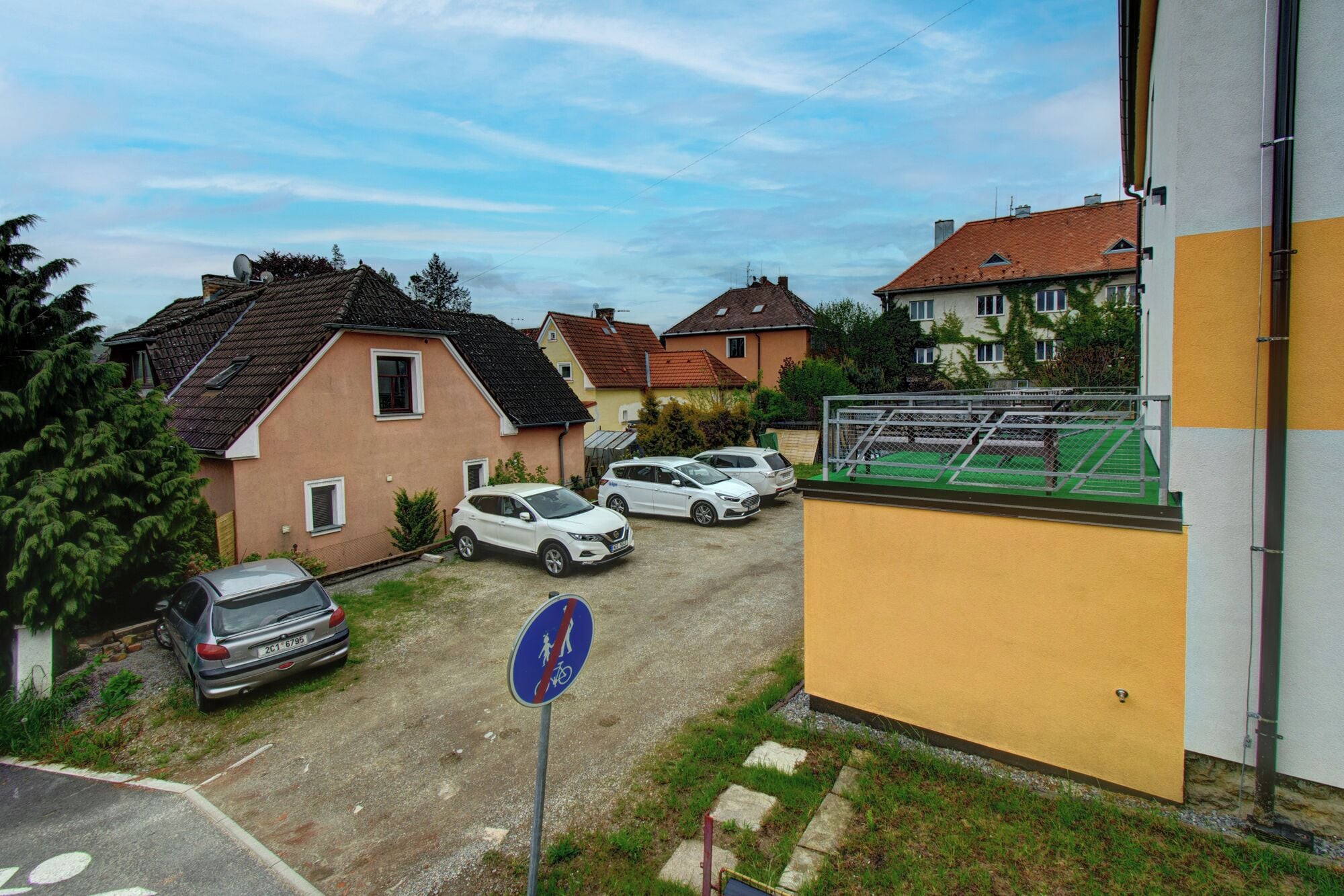 A residential street with houses, parked cars, and a no-parking sign.