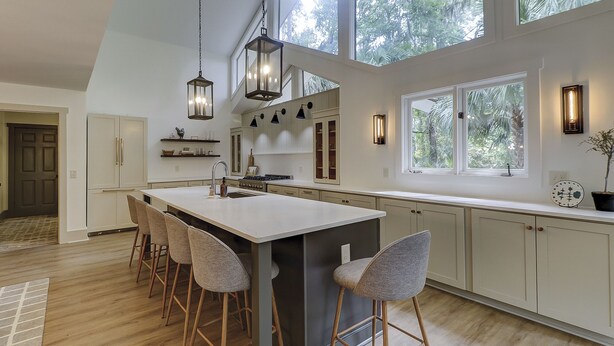Een moderne keuken met een groot eiland, barstoelen, hanglampen en grote ramen met uitzicht op het landschap.