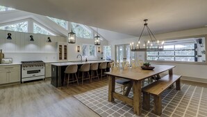 Een moderne keuken met een centraal eiland, barkrukken, een eettafel met banken en een kroonluchter.