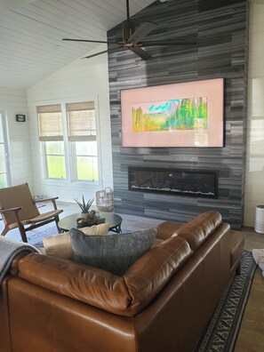 A modern living room with a leather sofa, a fireplace, a mounted TV, and a ceiling fan.