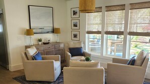 A living room with a sofa set, a coffee table, and a rug. There are two lamps, a painting on the wall, and a window with blinds. - Family Beach House - Pet-friendly - private heatable pool, close to the beach (Isle of Palms)