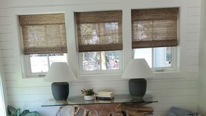 A room with a wooden floor, a large wooden table, two windows with woven blinds, a potted plant, and a small heater. - Family Beach House - Pet-friendly - private heatable pool, close to the beach (Isle of Palms)