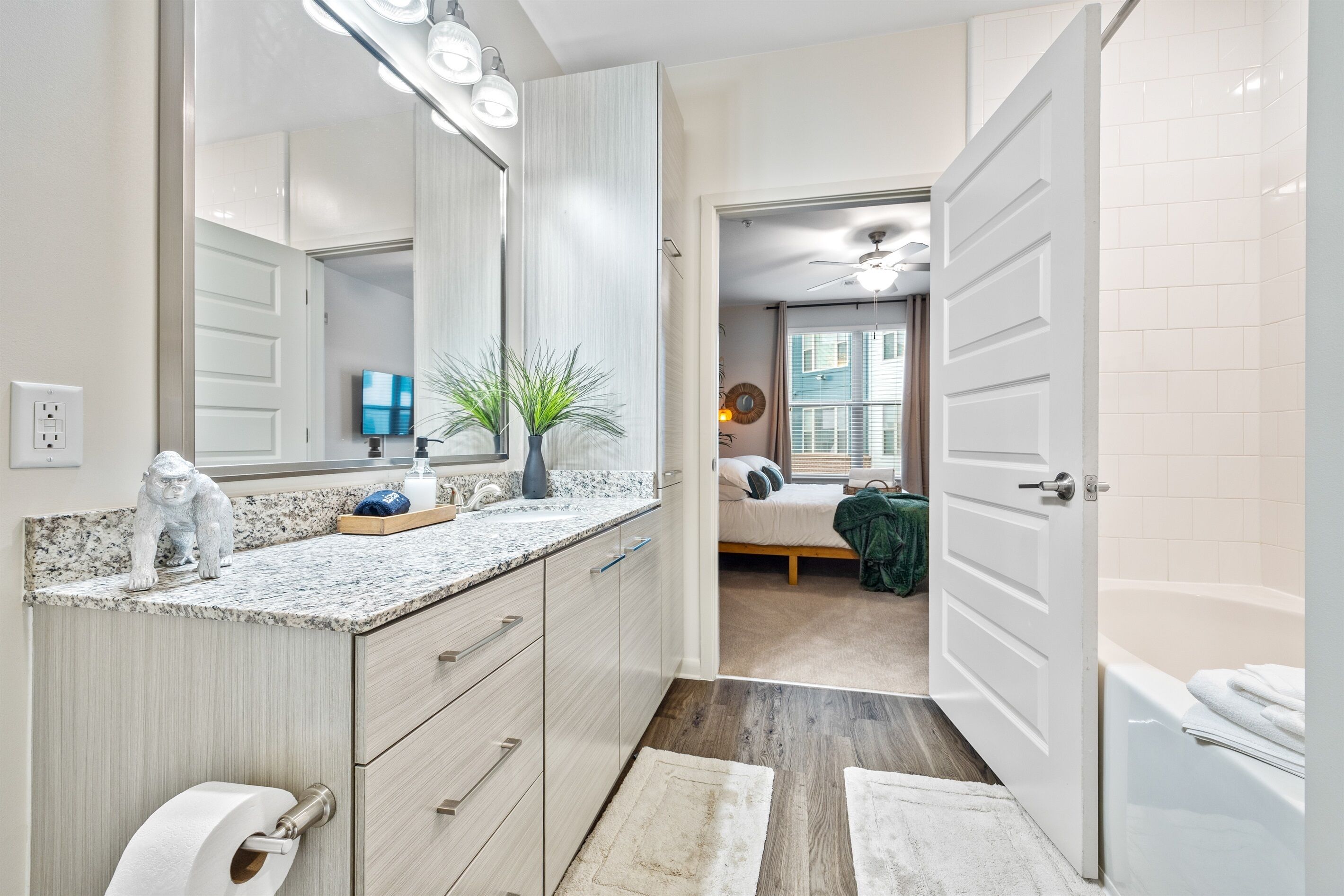 A modern bathroom with a large mirror, a toilet paper holder, and a sink with a granite countertop.