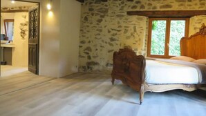 Un dormitorio con pared de piedra, estructura de cama de madera y ventana con vista a follaje.