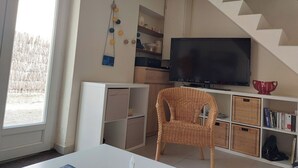 Ein Wohnzimmer mit Fernseher, Korbsessel und Treppe.