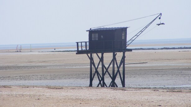 Ein hölzerner Aussichtsturm mit einem Kran auf einem sandigen Strand.