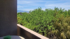 Uma varanda com vista para árvores verdejantes e montanhas ao longe, sob um céu claro.
