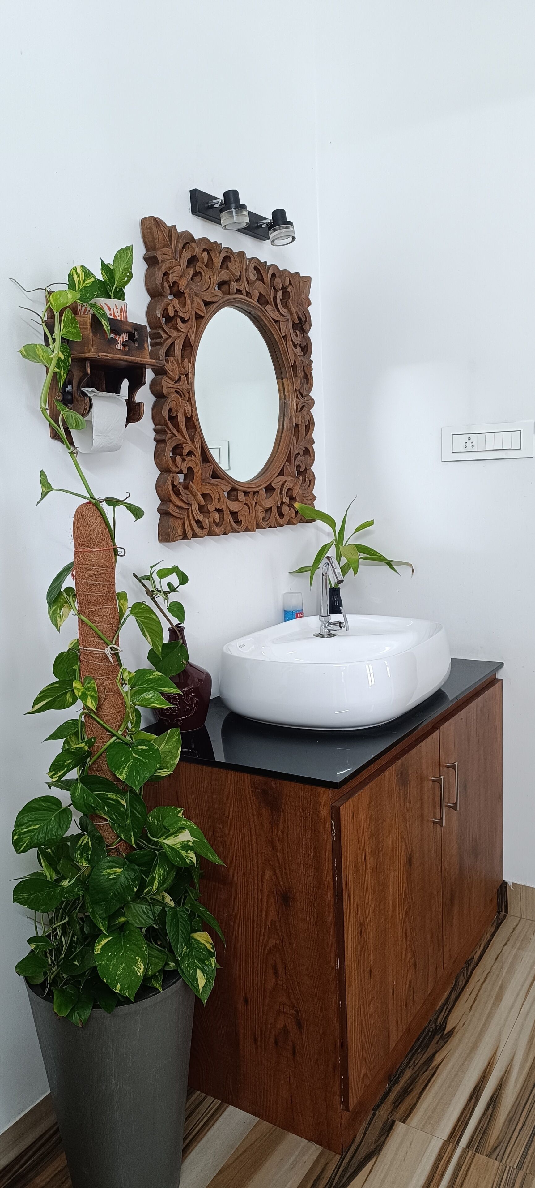 Un baño con tocador de madera, un lavabo blanco, un espejo con marco de madera y una planta en maceta.
