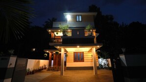Una casa a due piani con un balcone, piante in vaso e un ingresso ben illuminato.