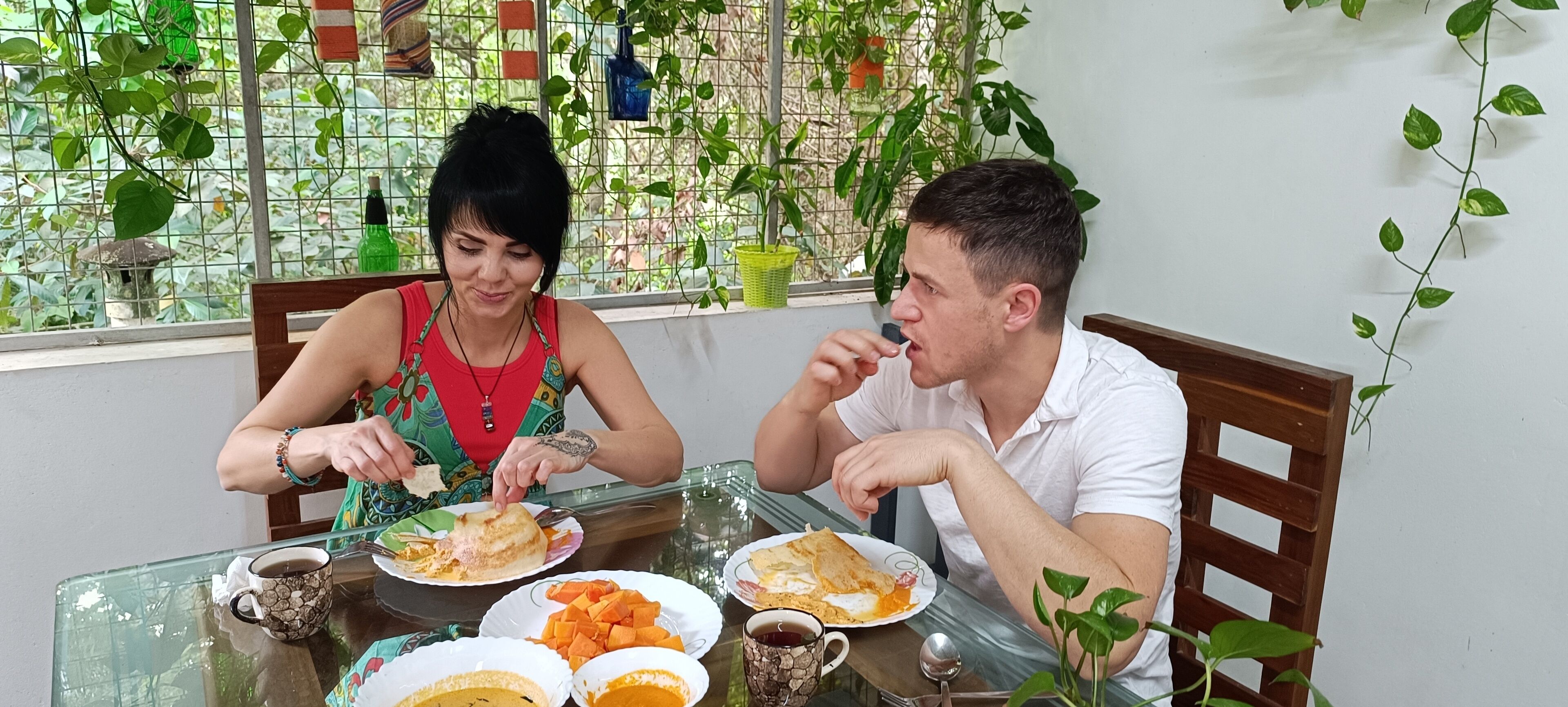 Deux personnes sont assises à une table, devant des assiettes remplies de nourriture, des tasses et une table en verre.