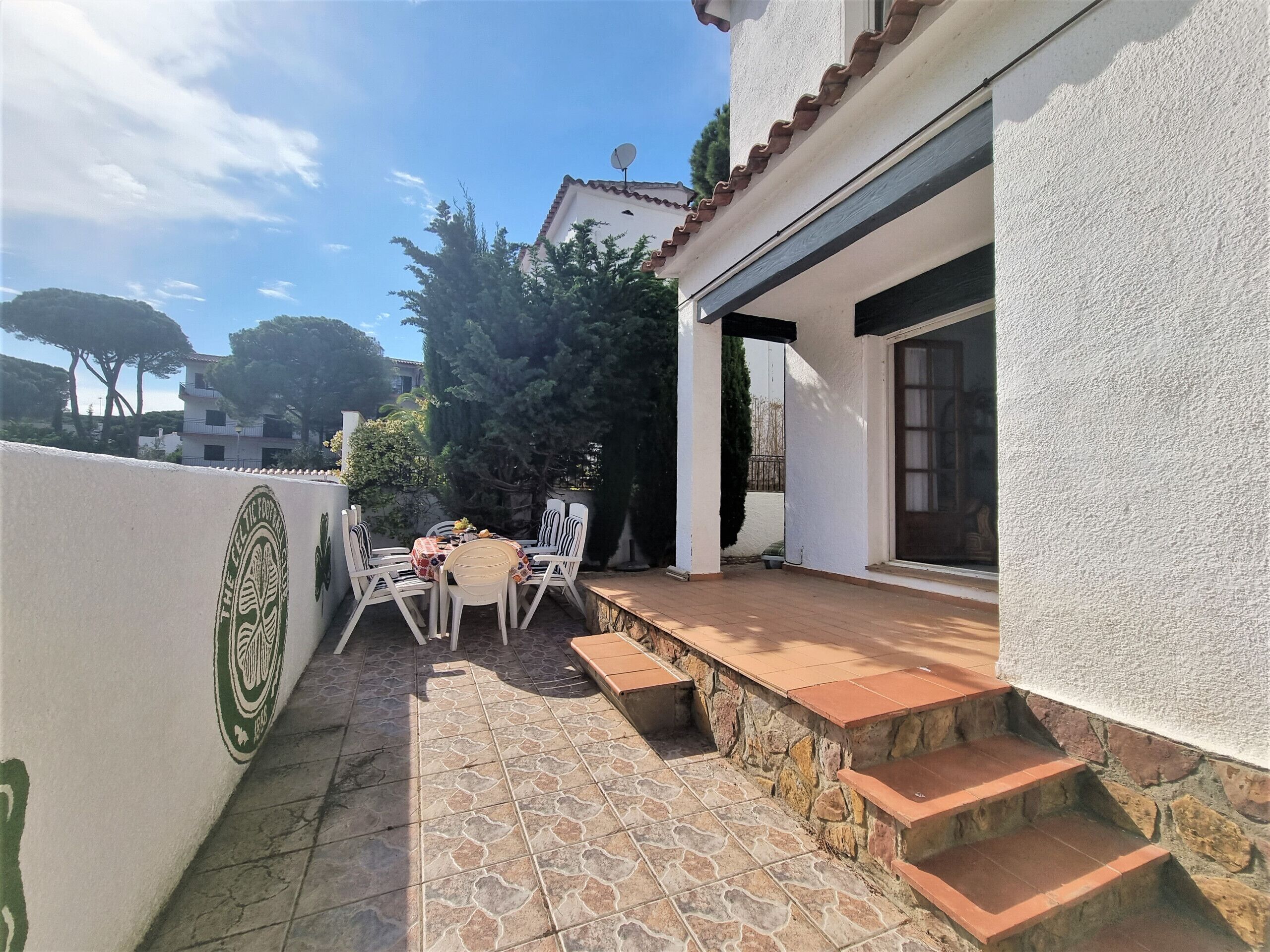 Un patio con una mesa y sillas, un muro de piedra y un edificio de fachada blanca con una antena parabólica.