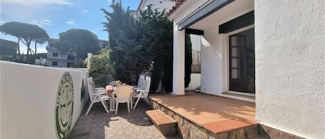 Um pátio com mesa e cadeiras, uma parede de pedra e um edifício com fachada branca e antena parabólica.