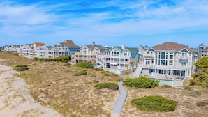 A beachfront property with multiple houses, a sandy path, and a small pool. - Premier Oceanfront w/ Private Pool, Hot Tub, Game Room, Putting Green, Theater (Hatteras)