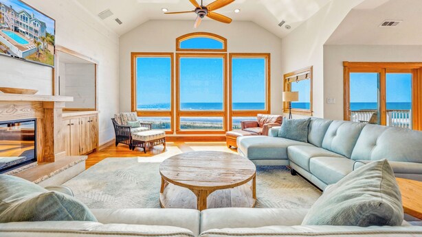 A spacious living room with a large window, a ceiling fan, and a view of the ocean. - Premier Oceanfront w/ Private Pool, Hot Tub, Game Room, Putting Green, Theater (Hatteras)