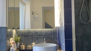 Ett badrum med ett runt handfat, en spegel, en dusch och en krukväxt.