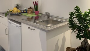 Ett modernt kök med vita skåp, en diskho i rostfritt stål och en köksfläkt. På bänkskivan står det citroner och en krukväxt.