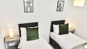 Camera d'albergo con due letti, ciascuno con cuscino e lampada da comodino. Alle pareti sopra i letti sono esposti dei quadri incorniciati.