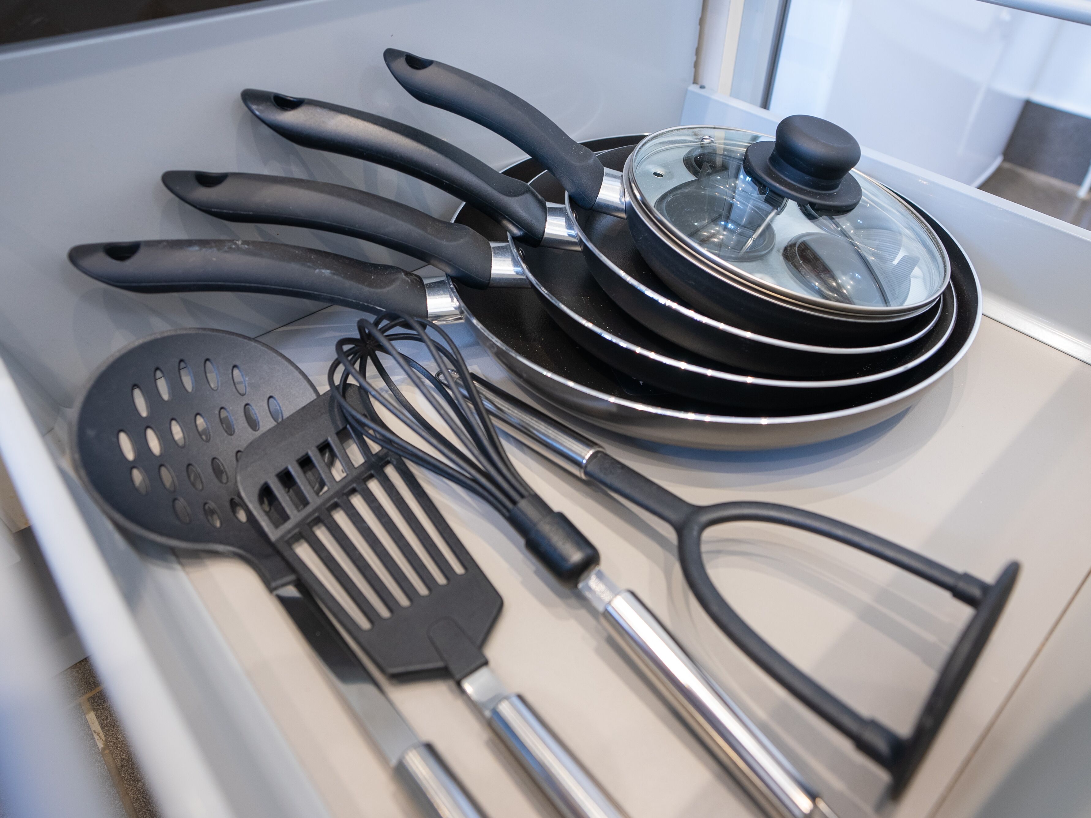 A kitchen drawer with various utensils including spatulas, whisks, and frying pans.