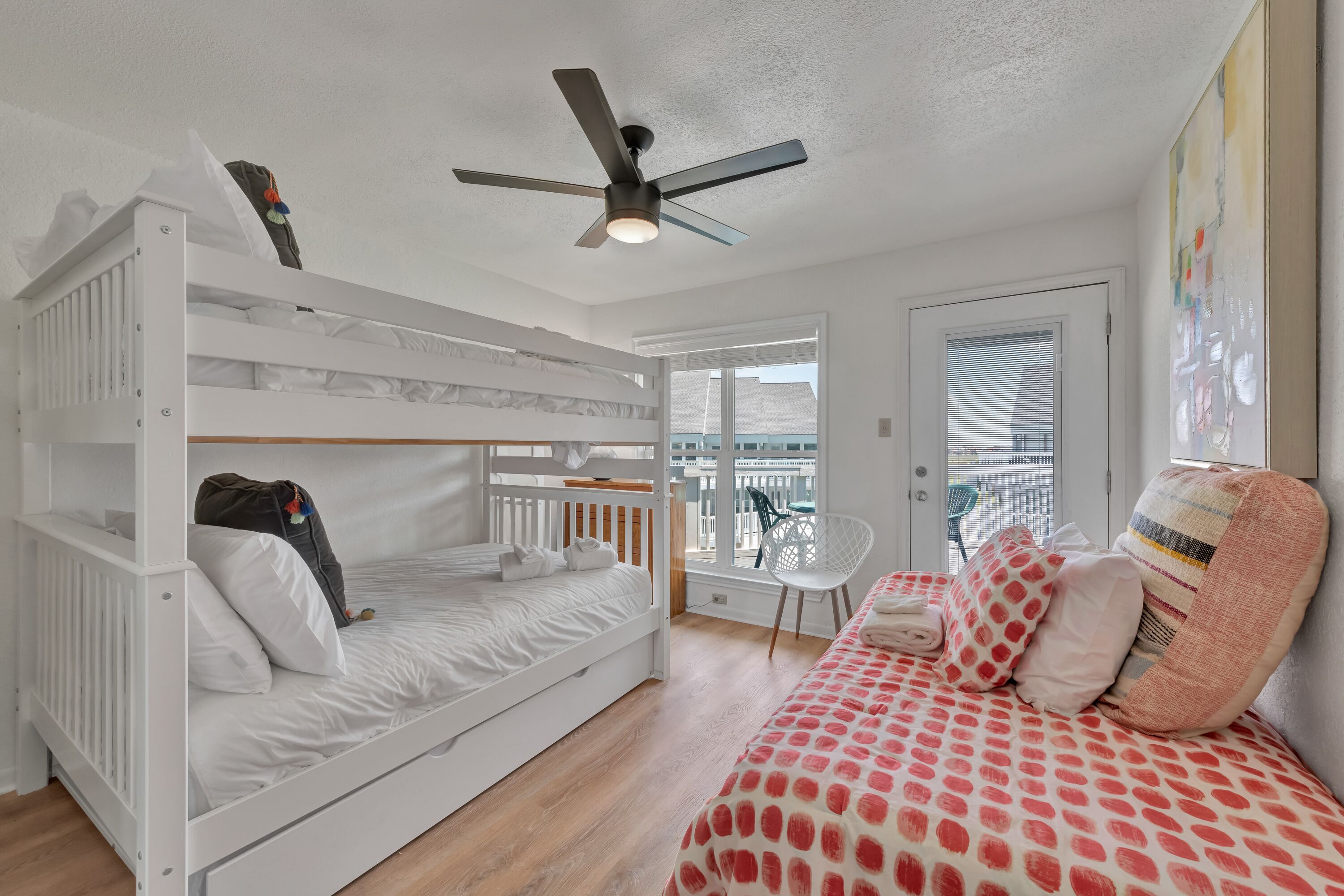Une chambre avec un lit superposé, un lit simple, un ventilateur de plafond et un balcon avec une chaise.