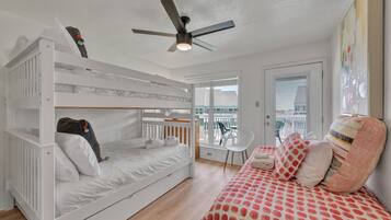 Une chambre avec un lit superposé, un lit simple, un ventilateur de plafond et un balcon avec une chaise.