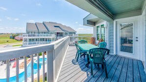 Une terrasse en bois avec une table et des chaises, une piscine et, au loin, une maison.