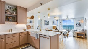 A modern kitchen with a central island, pendant lighting, and a view of the ocean through large windows. - Shoalwater 505 by Liquid Life (Orange Beach)