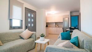 A modern living room with a sofa, a small table with a plant, and a kitchen in the background. - Onar Zin Seabliss - Iro Pool Bliss Getaway (Xilokastro)