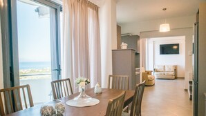 A dining area with a view of the sea, a sofa, and a TV in the living room.
