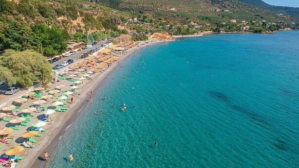 Une plage côtière aux eaux turquoise et limpides, avec des parasols et des gens qui se baignent.