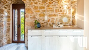 Une pièce aux murs de pierre, avec une porte en bois, une armoire blanche et un miroir accroché au mur.
