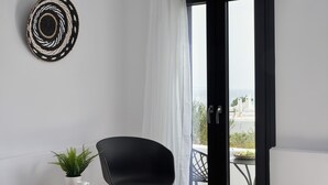 Een moderne kamer met een zwarte stoel, een klein houten bijzettafeltje met een plant en een boek, en een uitzicht door een glazen deur op een buitenbalkon.