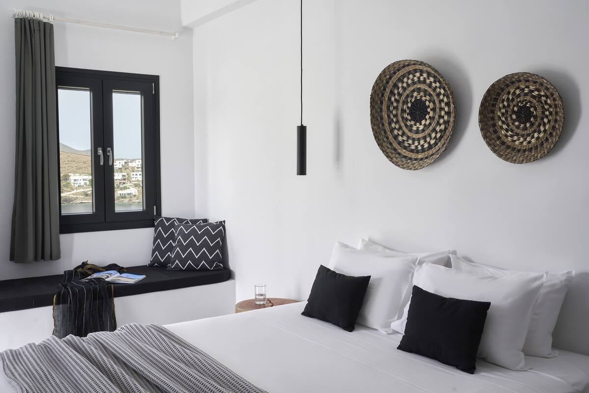 Un dormitorio con cama, un asiento junto a la ventana, una mesita de noche y dos adornos de pared tejidos.