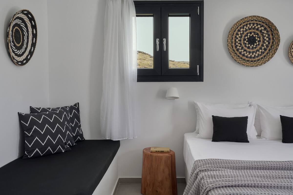 Un dormitorio con cama, almohadas, una ventana y una lámpara fijada a la pared.