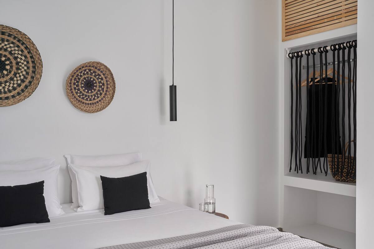 Un dormitorio moderno con cama, dos cestas circulares tejidas colgadas en la pared, una lámpara colgante y un armario con cuerdas negras.