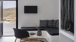 Een moderne woonkamer met een bank, een flatscreen televisie, een vaas met takken en uitzicht op een glooiend landschap door een groot raam.